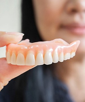 Woman blurry in background holding upper arch of dentures for foreground