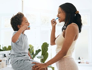 Woman and little boy facing each other brushing teeth