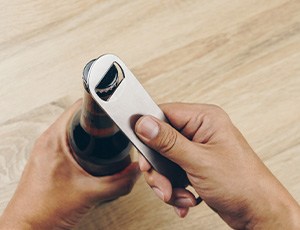 Hands using bottle opener to open glass bottle