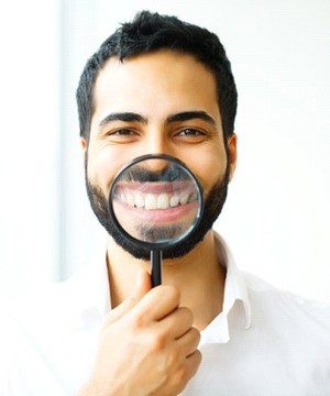 man in white shirt holding magnifying glass to his smile