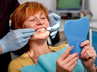 An older smiling woman admiring her dentures in a hand mirror
