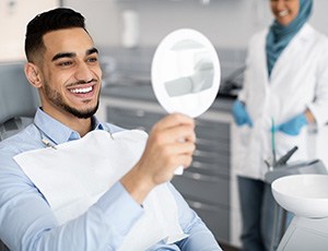 Man smiling at reflection in handheld mirror