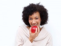woman with dental implants in Virginia Beach biting into a red apple 