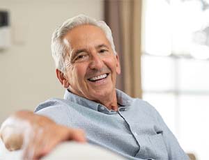 senior man with dental implants in Virginia Beach lounging on a couch