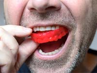 man putting a red mouthguard into his mouth