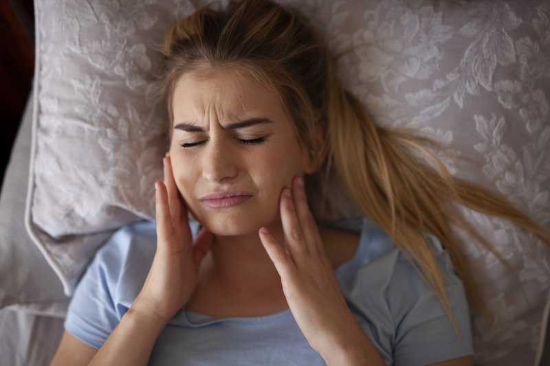 Woman experiencing jaw pain after grinding teeth at night