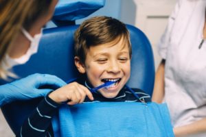 young boy brushing his teeth in dental chair