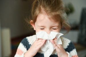 a child with a cold blowing her nose