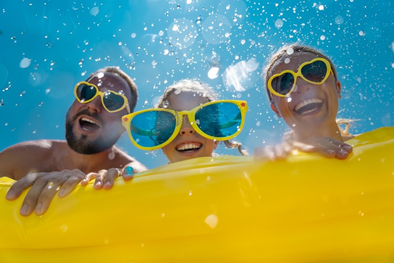 A man, child, and woman wearing yellow sunglasses on a yellow inflatable pool float