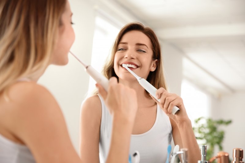 A woman brushing her teeth in the mirror after teeth whitening treatment