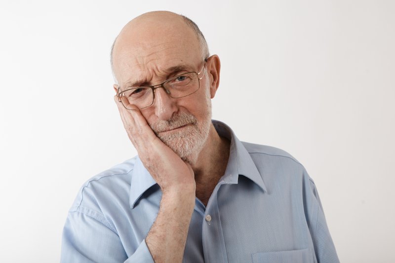 Older man holding his cheek due to denture sores