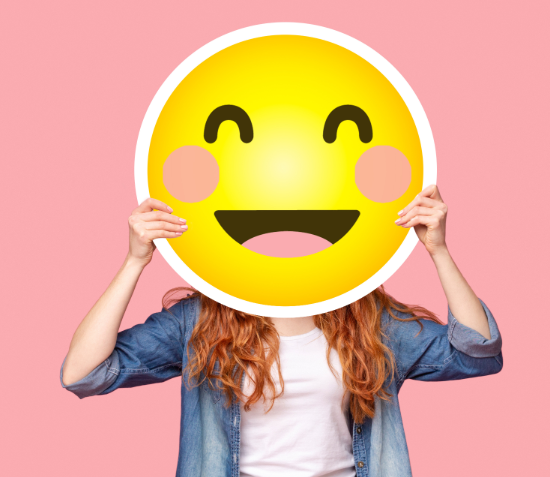 Woman holding smile emoji over face