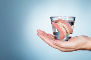 Hand holding dentures submerged in glass of water.